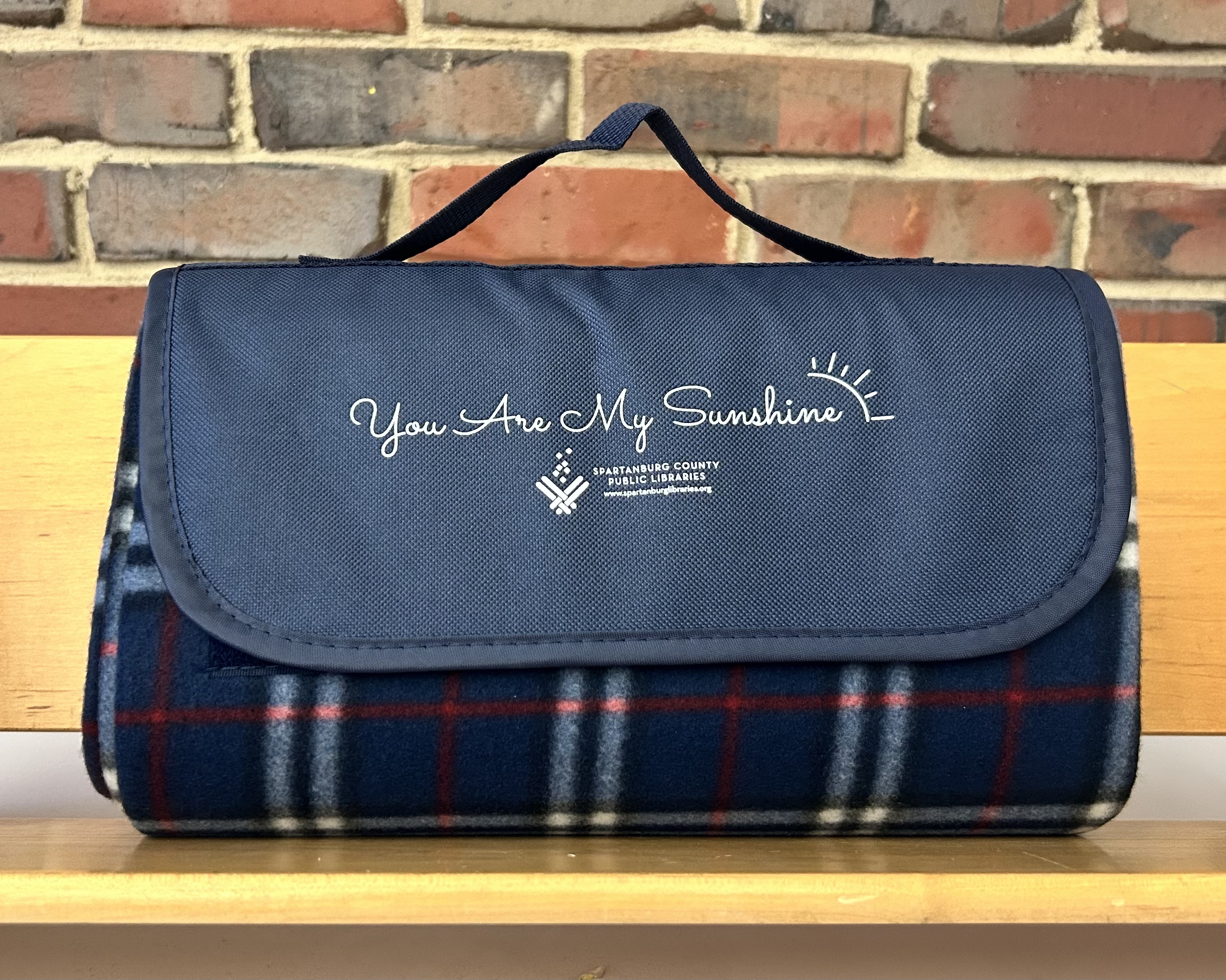 A blue, red, and white flannel blanket with You Are My Sunshine embroidered on one edge.